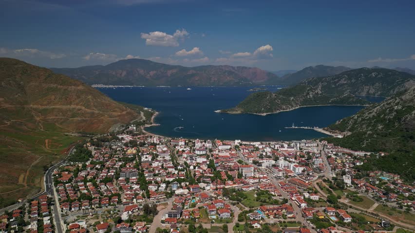 Scenic drone view of Icmeler, Turkey (Turkiye), coastal town nestled between lush hills and the Aegean Sea. Red rooftops, blue waters, and winding roads define this Turkish paradise.