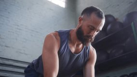 Concentrated bearded man in gray tank top performing dumbbell bent over row exercise with proper form in bright industrial fitness space with white brick walls - Powered by Shutterstock - Get 15% off with code: PIKWIZARD15
