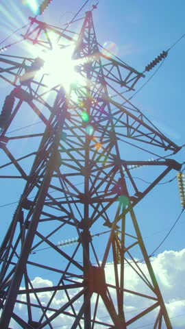 High-voltage supports with wires and insulators against the background of blue sky and flying clouds. Transmission of electricity by wires. Vertical video.