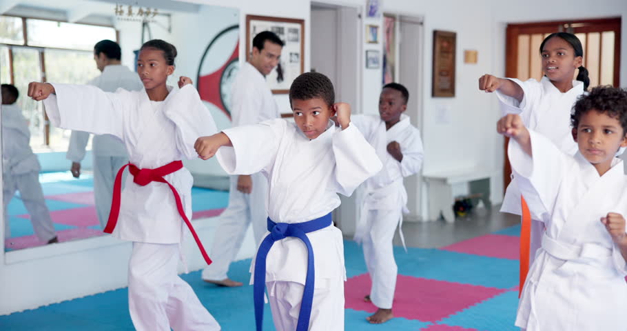 Kids, learning karate and training in class with instructor for fight, fitness or self defense. Students, children and people practice martial arts, kick and exercise for lesson with teacher in dojo