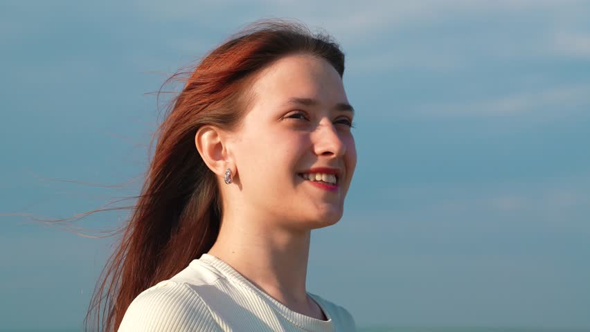 Portrait of smiling girl sunny day, sky. Beautiful flowing female chestnut hair. Young woman looking at sky, person. Girl's hair fluttering in wind, faith in goodness, romantic woman dreams of love