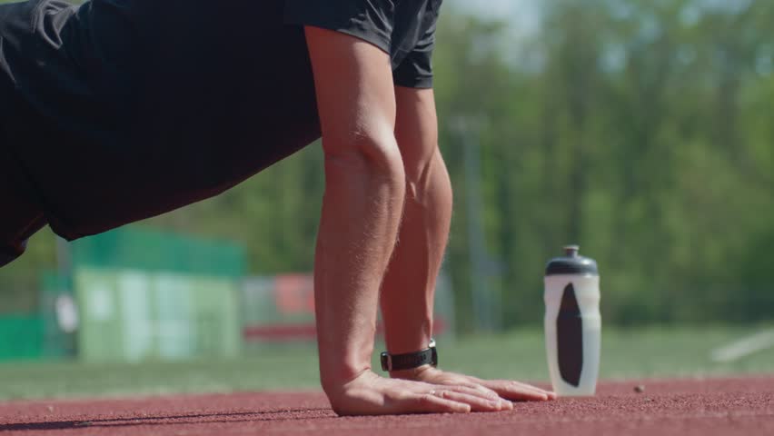 Athletic man doing push-ups on red running track with water bottle nearby. Outdoor workout session. Person training on stadium. Active lifestyle, sport and fitness concept - Powered by Shutterstock - Get 15% off with code: PIKWIZARD15