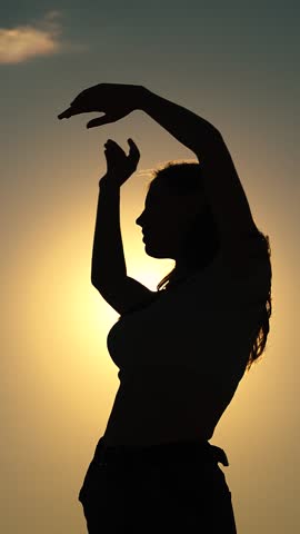Beautiful girl dancing cheerfully on summer evening, sun. Teenager dancing cheerfully with raised hands to music. Celebrate summer day beach party. Having fun beach party in front of sunny sky, sunset