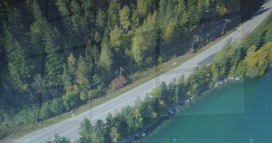 Two dark sedans traveling along asphalt road through forest beside teal lake showing HUD overlay. Nature, transportation, adventure, exploration, outdoor, scenic, technology