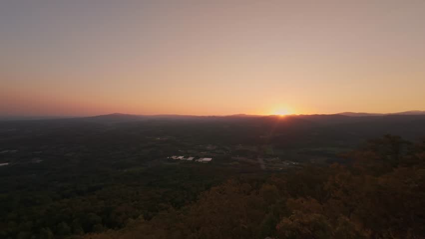 Drone view of sunrise over Buffalo Mountain Tennessee casting golden light across forested landscape and distant river under warm gradient sky USA, Buffalo Mountain