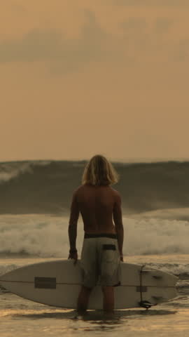 Slow Motion Surfer Standing In Ocean Holding Surfboard Watching Sunset Waves Vertical Wide Shot Athletic Blond Man Waiting Surf Moment Serene Mood Freedom Vibes Training Scene Nature Power