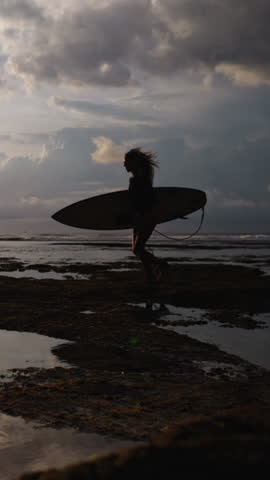 Slow Motion Female Surfer Running On Beach With Surfboard Reflection In Water During Sunset Vertical Wide Shot Golden Hour Coastal Mood Freedom Movement Sporty Elegance Ocean Lifestyle Scene