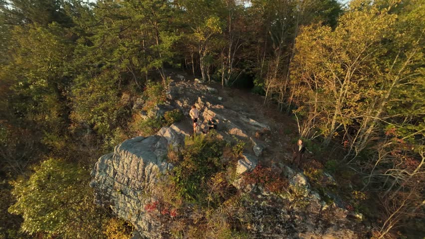 Hikers standing on rocky cliff edge surrounded by autumn trees on Buffalo Mountain at golden hour Hikers on rocky cliff Adventurers standing on Buffalo Mountain Tennessee cliff edge by fall forest