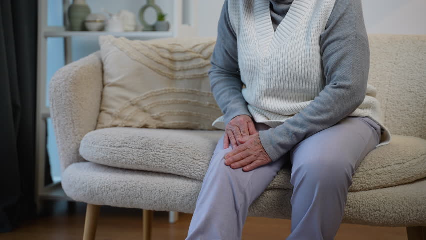 Pensioner suffering from knee pain while sitting at home