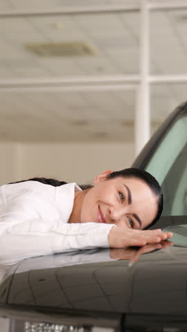 Joyful woman hugging new car in showroom