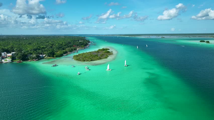 Drone circles around boats sailing on emerald green lagoon under blue sky, Lagoon of seven colors, Bacalar, Quintana Roo