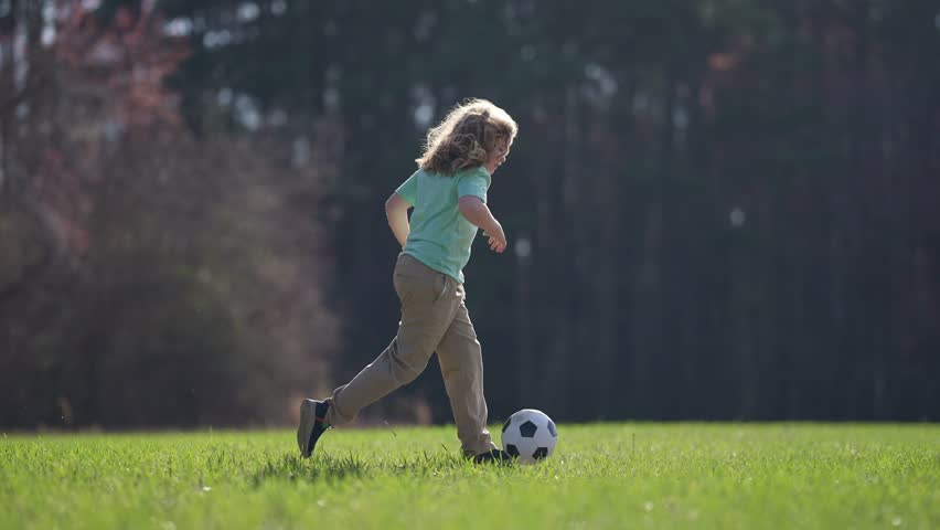 Kid playing football. Kid boy kicking a football on the grass. Kid running with a soccer ball. Playful children enjoying a football game. Kids soccer match. Kid playing football kicking ball.