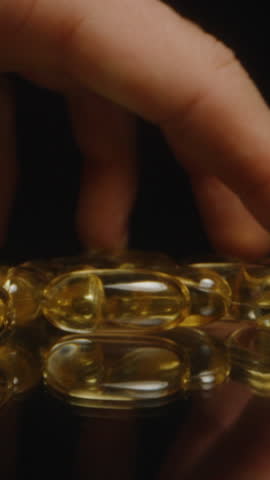 Vertical video. Fingers Picking Up a Golden Transparent Capsule from a Reflective Surface Displaying Smooth Texture and Shiny Appearance Healthy Living