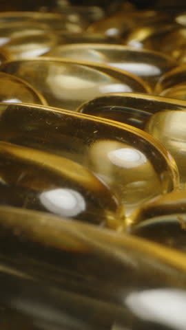 Vertical video. Dolly Slider Close Up of Golden Transparent Omega 3 Fish Oil Capsules Highlighting Their Smooth Shiny Surface and Reflective Details Nutritional Supplementation