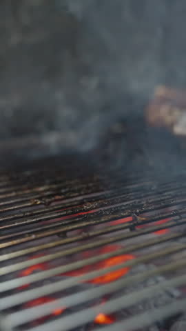 Vertical video. Slow motion A Fork Pressing Down on a Charred Steak Cooking Over Red-Hot Coals Surrounded by Smoke Highlighting Its Juicy Texture Barbecue Cooking