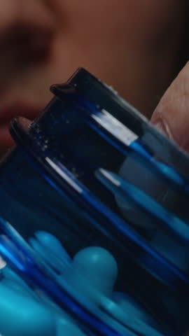 Vertical video. A Man Picking a White Capsule from an Open Blue Bottle Showing the Smooth Surface and Precise Shape of the Pill Nutritional Supplementation