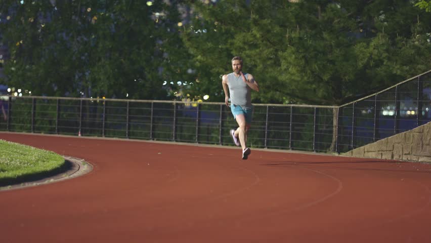 Sports man running in stadium. Sportsman in action during race. Runner in downtown streets. Sprinting athlete man. Man runs at night stadium. Sprinter man running on stadium.