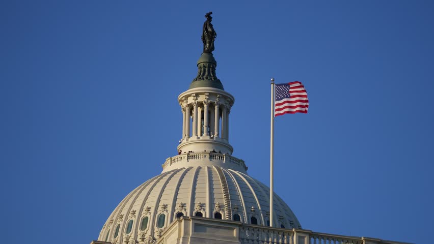 American flag waving near Congress Capitol dome in Washington DC. USA symbol. United States flag on Capitol. Flag against sky in Capitol. Flying American flag. Vote for freedom. Capitol Hill flags.
