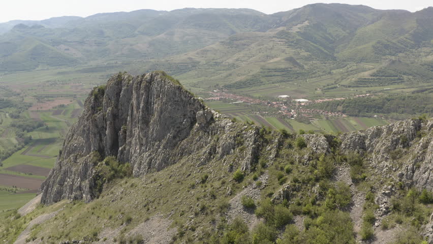 Flyover above peak of Piatra Secuiului in Romania, revealing fertile farmland in valley below, near villages of Rimetea and Pietroasa