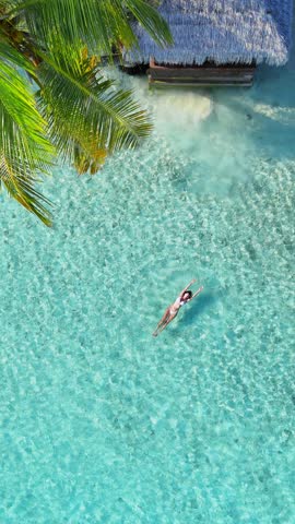 Calm vertical paradise aerial view, Tropical white sand beach with turquoise water and palm trees, woman floating, swimming, serene atmosphere for summer travel, hotel, resort, family vacation