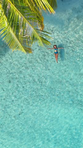 Calm vertical paradise aerial view, Tropical white sand beach with turquoise water and palm trees, woman floating, swimming, serene atmosphere for summer travel, hotel, resort, family vacation