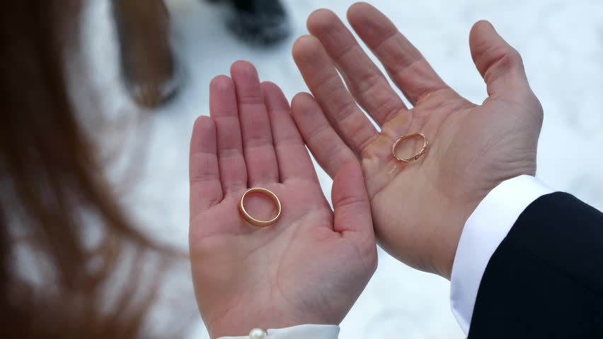 The bride and groom hold wedding rings in their open hands