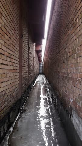 Icy industrial area factory corridor between two brick walls with strong vertical perspective and daylight above.