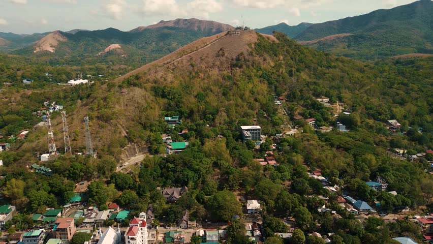 Drone footage of Mount Tapyas in Coron, Palawan, rising above a green townscape. The iconic hilltop viewpoint, with telecom towers and winding paths, offers a panoramic look at island life.