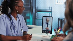 African american nurse making a videocall with doctor to chat with patients, doing a remote check up and telemedicine concept. Skilled medical assistant asks opinion of a specialist. Camera B. - Powered by Shutterstock - Get 15% off with code: PIKWIZARD15