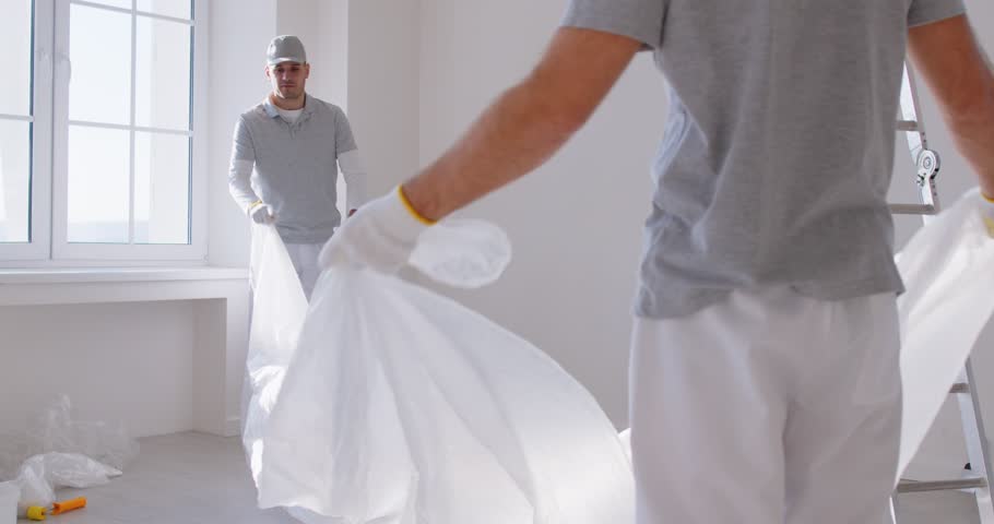 Slow motion video of young painters preparing empty room for painting during repair of new apartment. Team of building contractors renovating house. Renovation and repair service concept. 4k video.