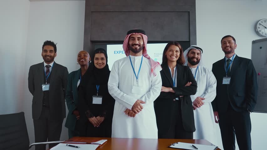Multicultural businesspeople wearing suits and traditional clothing stand together in a modern office, embodying teamwork and cultural diversity.