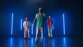 Three talented dancers, two women and a man, showcase their impressive moves on a dark stage illuminated by vertical blue neon lights, creating a vibrant and dynamic performance - Powered by Shutterstock - Get 15% off with code: PIKWIZARD15