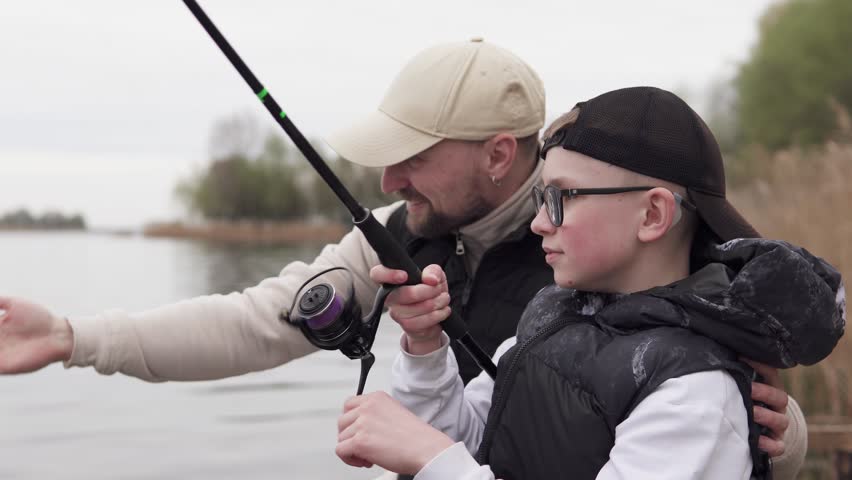 Father and son fishing on a wooden pier. Father teaching his child to fish. Fatherhood concept.