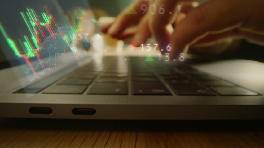 Up Close with Person's Hands Working on a Laptop Computer. Animated Holograms Present Upward and Downward Trending Stock Market Icons and Graphs. Economy, Finance and Investing Concept