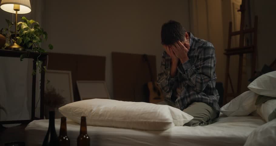 Man Falls Face Down On Pillow And Punches Up Mattress Lying On Mattress Near Empty Alcohol Bottles During Despair And Alcohol Addiction At Home