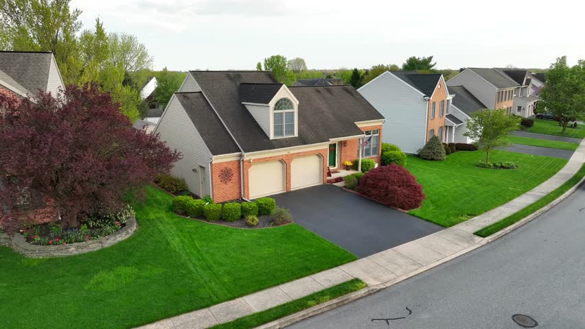 American Single Family House with double garage and american flag on facade. Green grass on front yard. Aerial approaching shot.