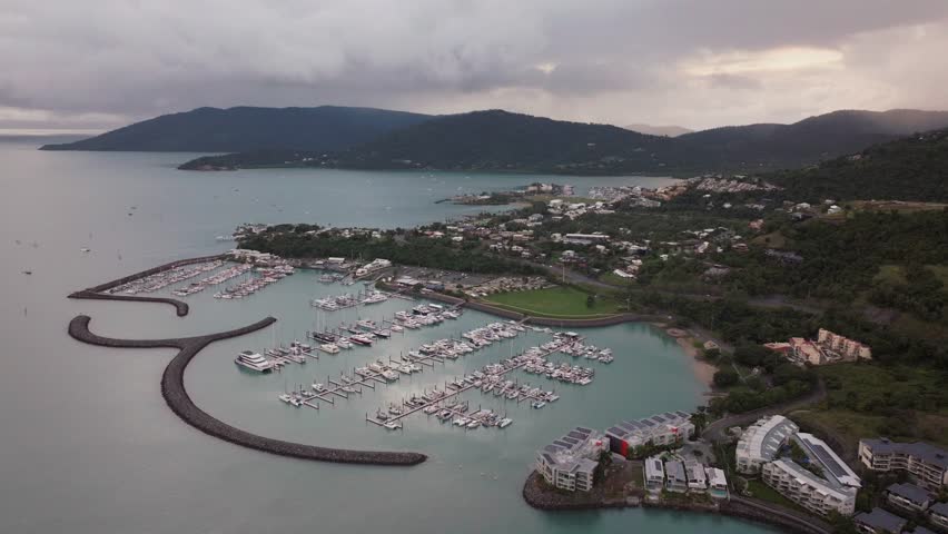 Port Airlie Beach Bay Lagoon Coral Sea marina aerial drone rain clouds mist sunrise morning heart of Great Barrier Reef Whitsundays Whitehaven jetty yachts sailboats buildings backward motion