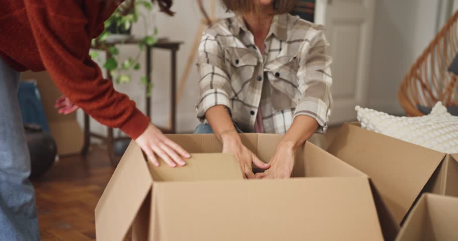 Up close dynamic scene of friends moving and packing furniture into cardboard boxes at home