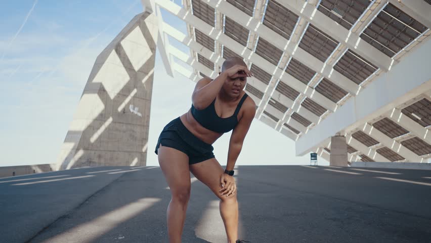 Muscular plus-size athlete standing confidently against concrete wall, embodying strength, determination, and body positivity with intense gaze and crossed arms in urban setting