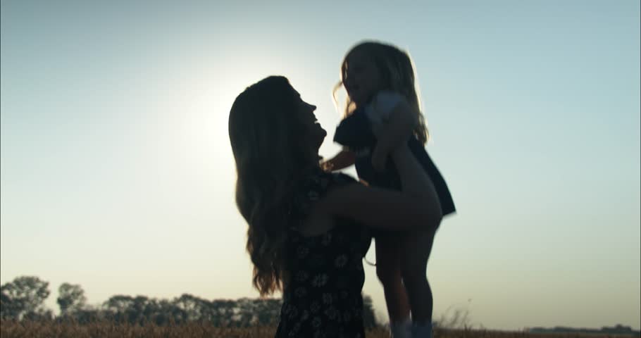 Silhouette of a happy mother and daughter playing, laughing, smiling together outside in summer sunset having positive, loving family or mothers day moment in cinematic slow motion.