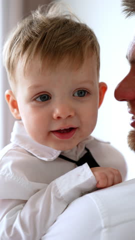 Adorable baby boy in white shirt and black tie is in dad