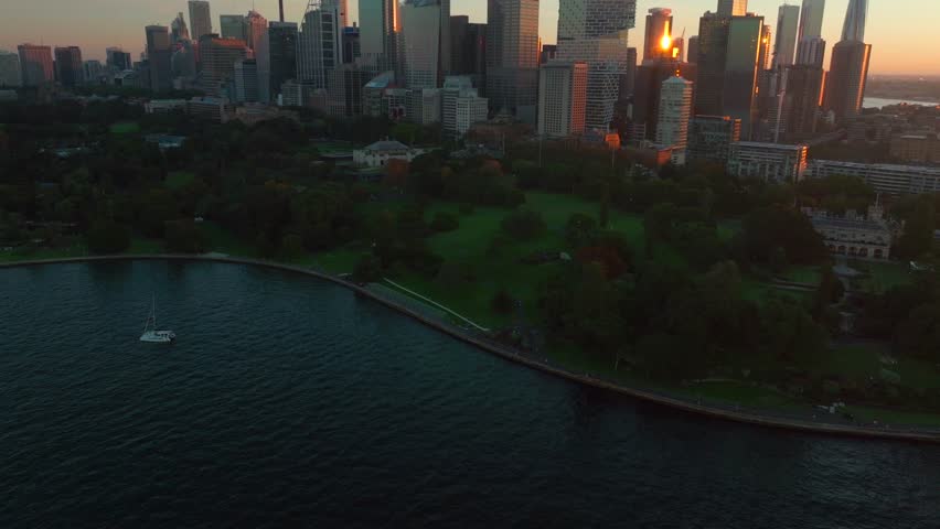 Sydney Eye Tower city skyline Royal Botanic Gardens Vivid summer sunset Australia aerial drone view tourist city Circular Quay scenic helicopter flight sailboat ferry boats orange forward pan up