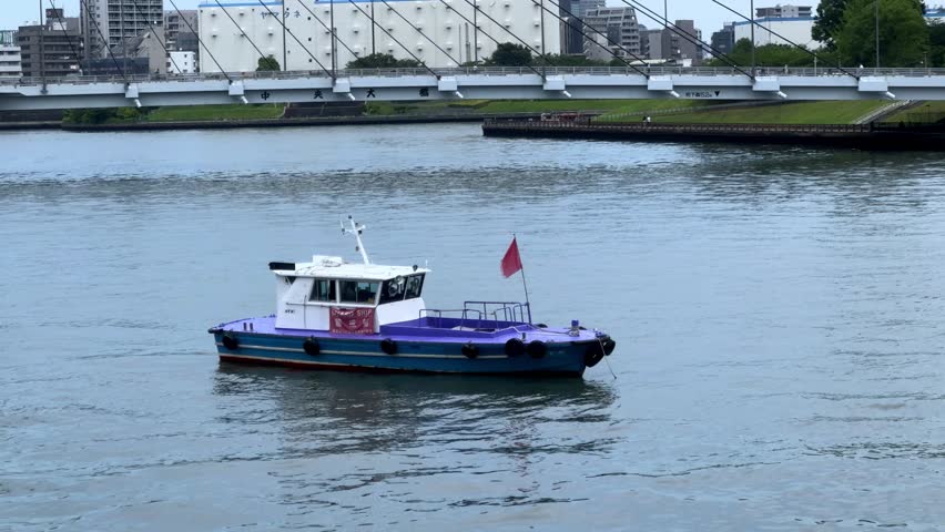 A small boat with a red flag floats on a calm river near an urban area