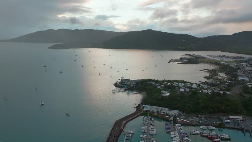 Port Airlie Beach Bay Lagoon Coral Sea marina aerial drone mist sunrise morning rain clouds heart of Great Barrier Reef Whitsundays Whitehaven jetty yachts sailboats circle right motion