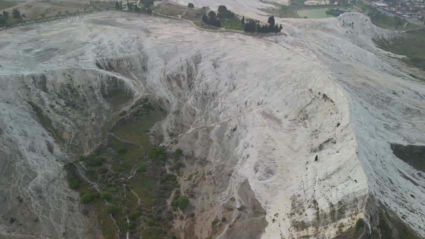 Panoramic retreat above Pamukkale, Turkiye. Drone captures elevation over calcium deposits. Widespread white terrain and thermal pools.
