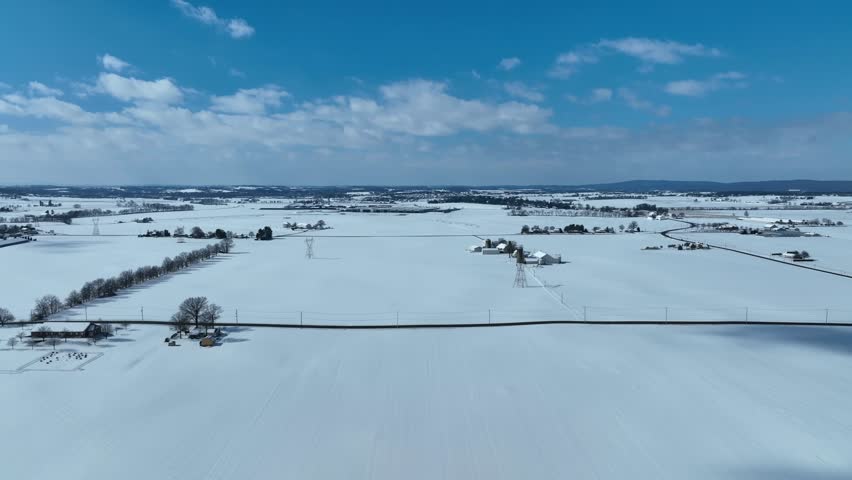 Aerial lateral wide shot of snowy winter landscape in rural area at sunny day. White winter snow coverding village neighborhood in USA. Panorama view.