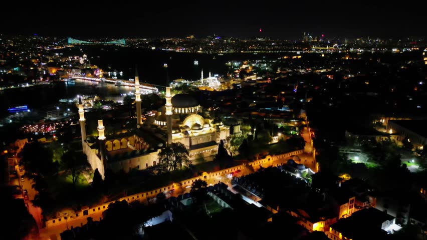 Stunning aerial night view over Suleymaniye Mosque in Istanbul, Turkey. City lights shimmer along the Bosphorus. Minarets and domes are beautifully illuminated.