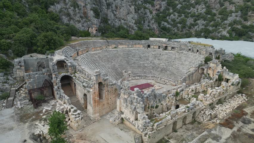 Myra's Roman theater in Turkiye shines in semicircle view. Tombs carved in cliffs nearby. Turkiye's past still visible in stonework and layout. Ancient stories echo in the valley.