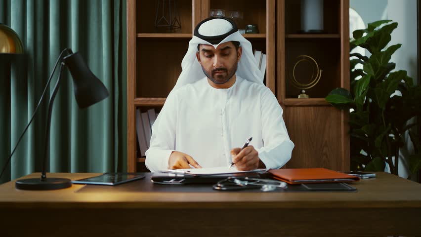 Professional emirati businessman wearing white kandura, working diligently on laptop in modern office, showcasing technological expertise within sleek corporate environment - Powered by Shutterstock - Get 15% off with code: PIKWIZARD15