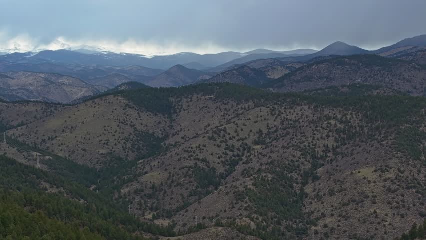 Evergreen trees cover sloping hillside of rocky mountains under overcast stormy sky in Colorado